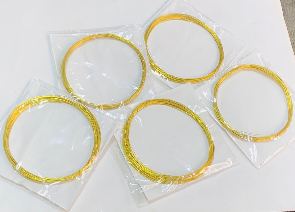 Five coiled gold wire springs, individually sealed in clear plastic bags, arranged on a plain white surface.