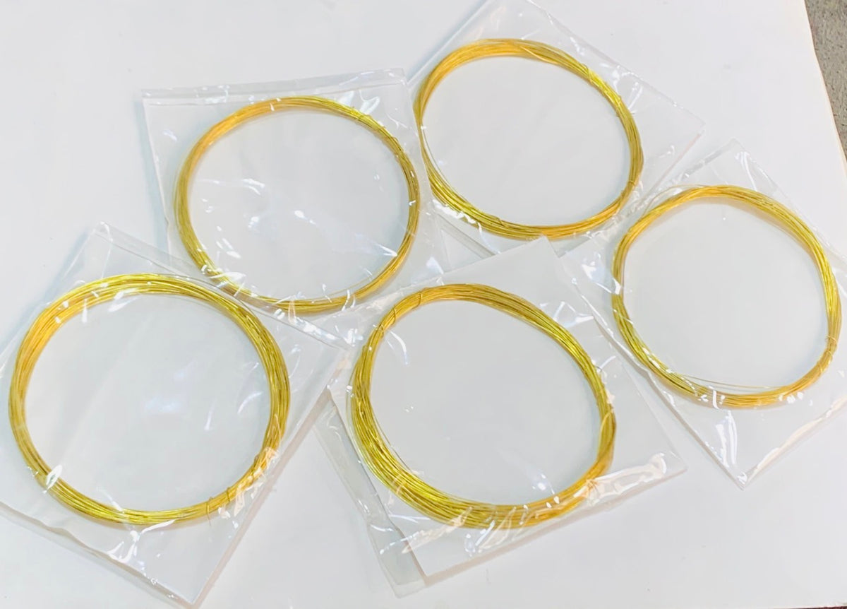 Five coiled gold wire springs, individually sealed in clear plastic bags, arranged on a plain white surface.