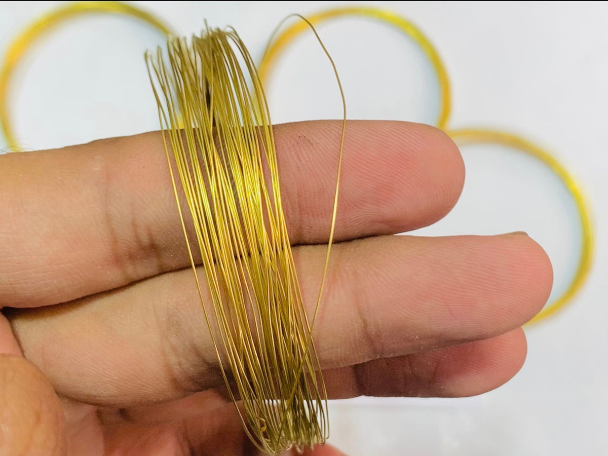 A hand holding a bundle of thin, shiny gold-colored metal wire, with blurred circular gold rings in the background.