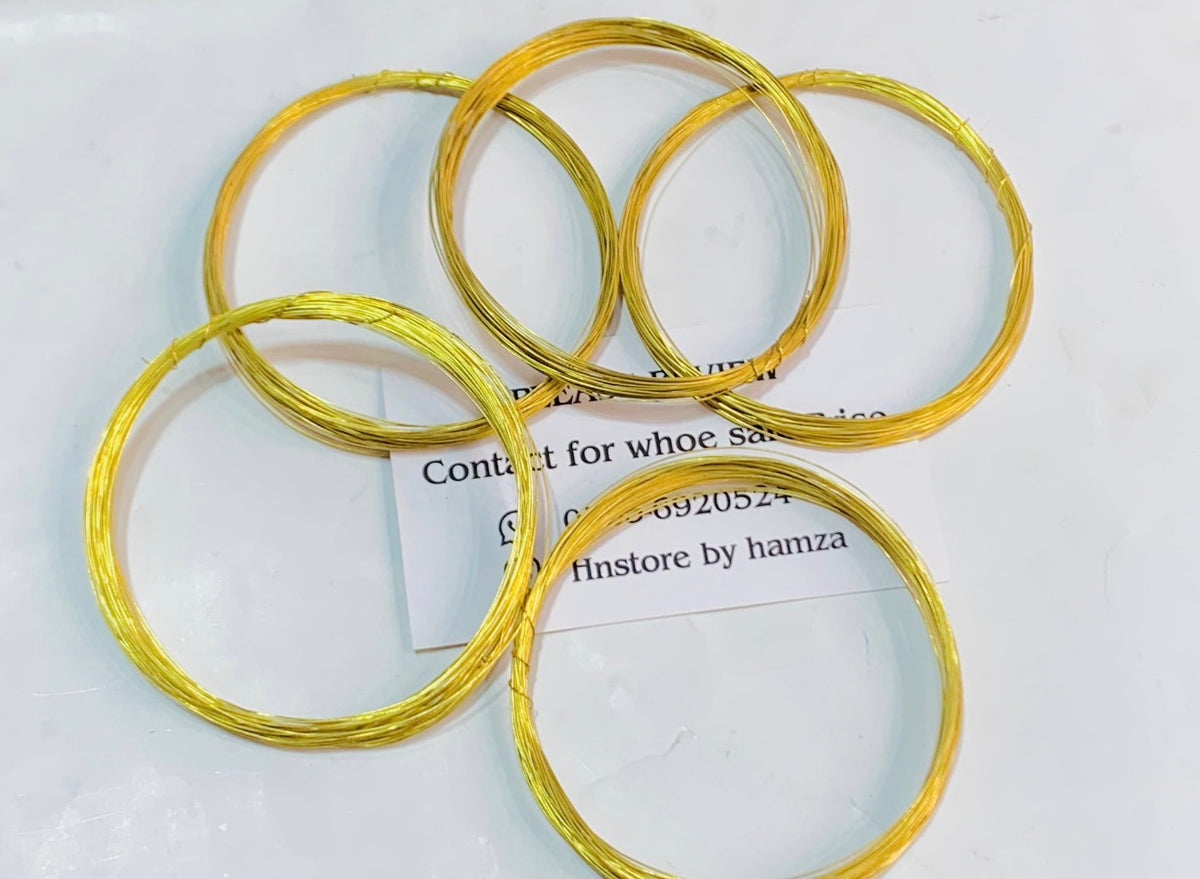 Five coiled gold wire rings of varying sizes arranged on a white surface with a small contact card underneath.