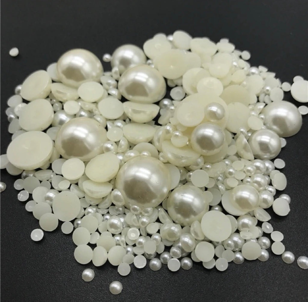 A pile of white faux pearl beads and flat round pearl discs in various sizes, displayed on a dark gray background.