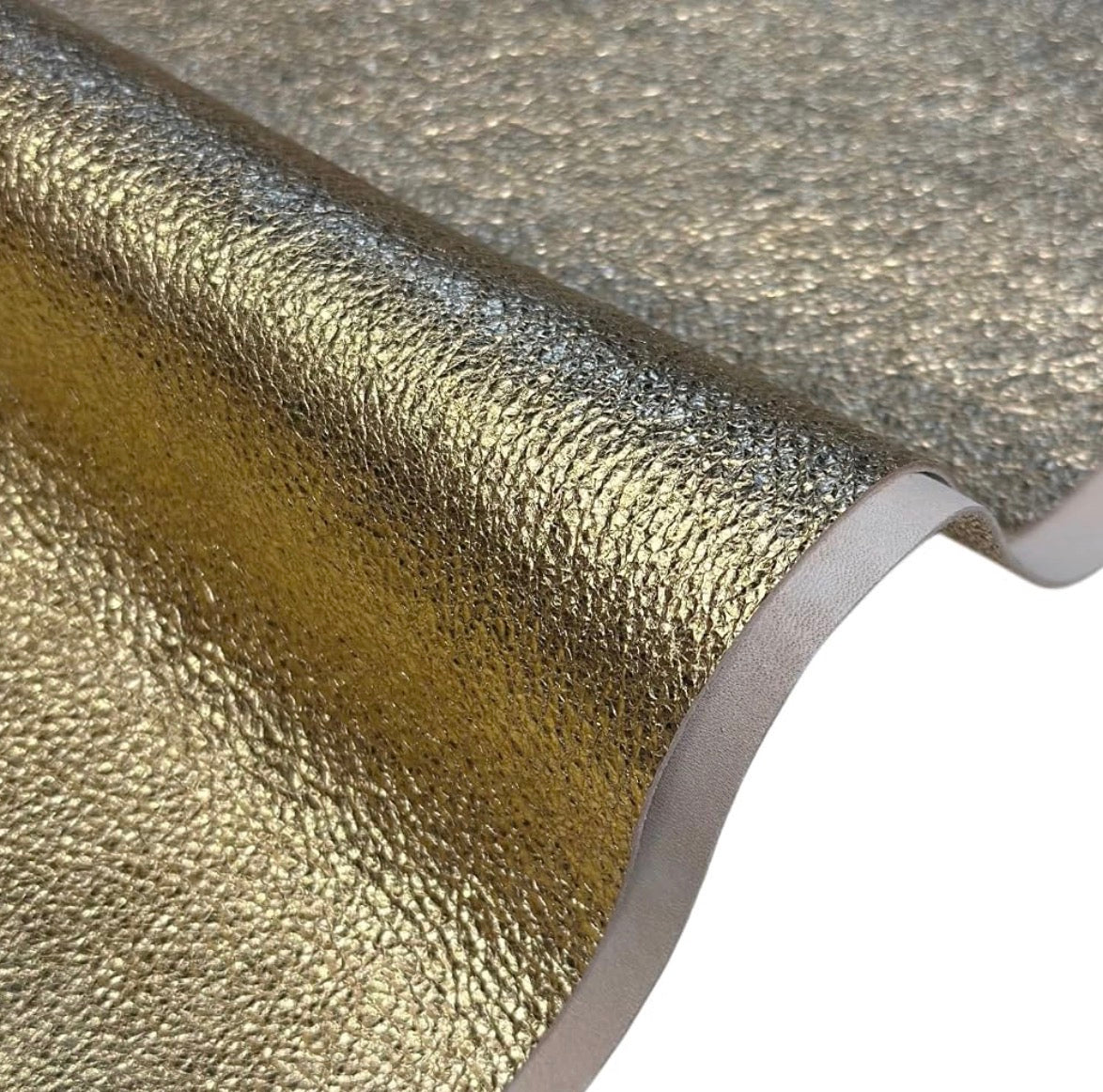 A close-up of a textured metallic gold material, likely a vinyl wrap, adhesive film, or wallpaper, shown with a curled edge revealing a white backing layer against a white background.