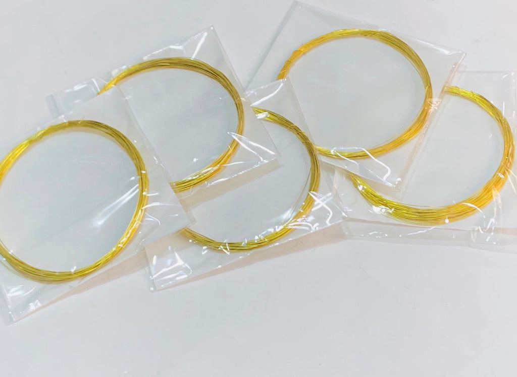 Four gold-colored metal wire loops, each sealed in a small clear plastic bag, arranged on a plain white surface.