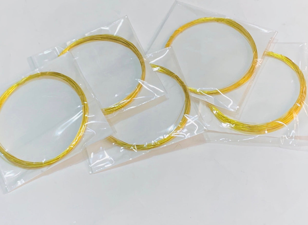 Four gold-colored metal wire loops, each sealed in a small clear plastic bag, arranged on a plain white surface.