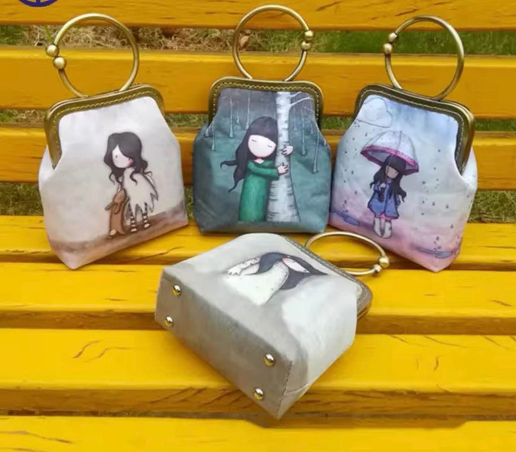 Four small kiss-lock coin purses with metal rings, displayed on a yellow wooden bench. Each purse has a different pastel illustration of a girl, including one with a dog, one in the rain, one under a umbrella, and one with a penguin.
