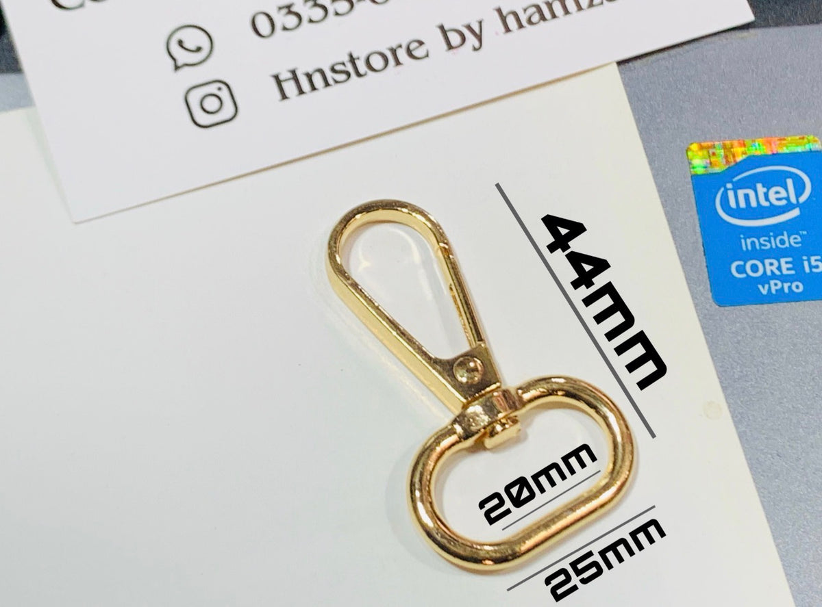 A gold-colored metal lobster clasp with a heart-shaped ring, shown on a white background with printed dimensions (44mm, 20mm, 25mm). A blue Intel Core i5 vPro sticker is visible on the right, and a card with social media contact info is partially visible at the top.