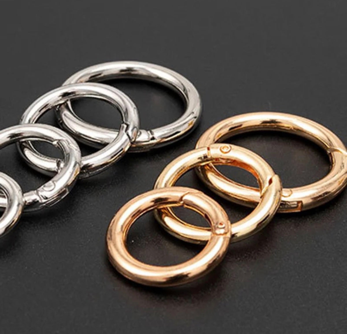 Four polished metal split rings, two silver-toned and two rose gold-toned, arranged on a dark gray background.
