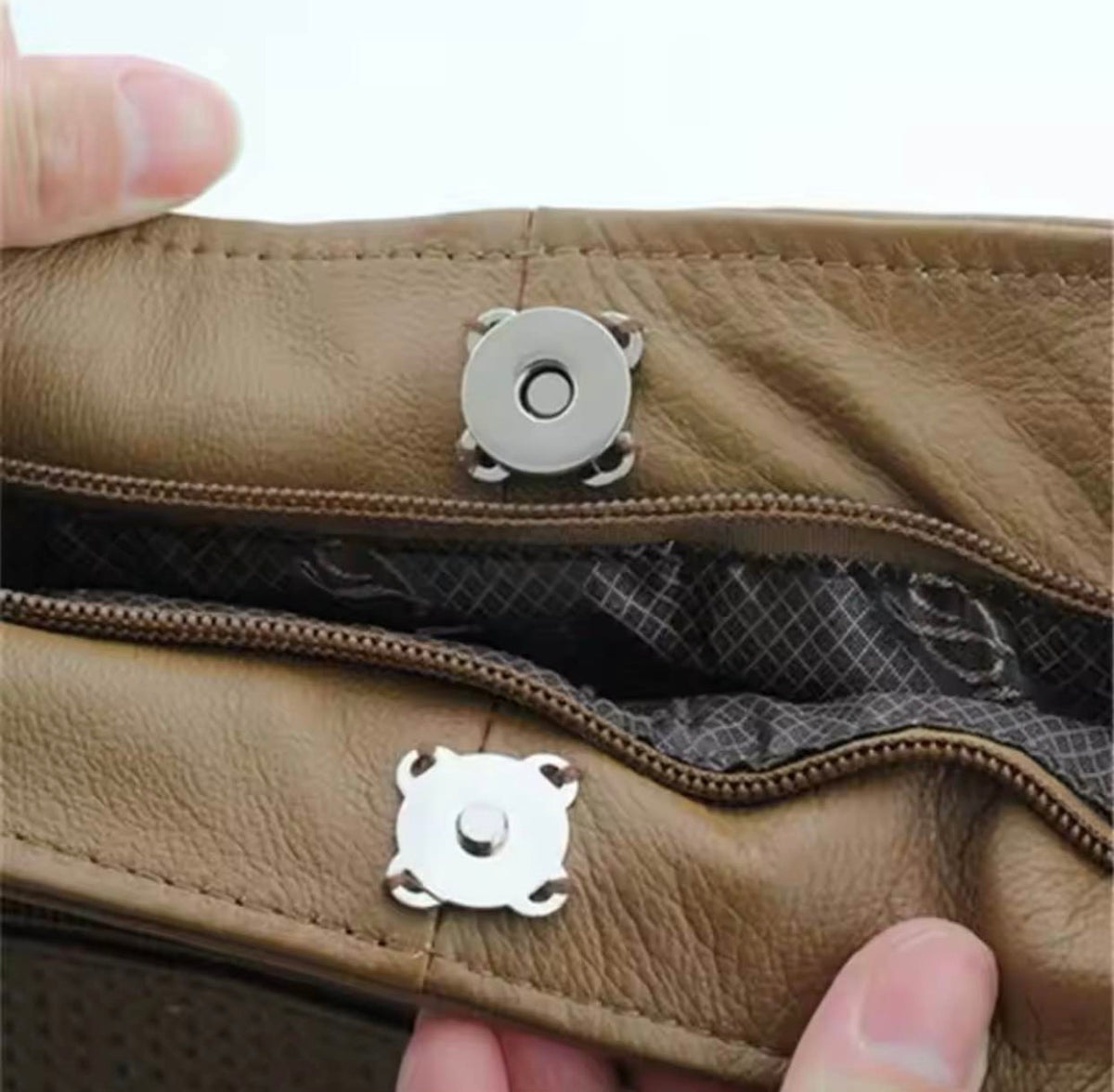 Close-up of a tan leather zippered pouch or wallet being held by hands, showing a silver snap button closure and the interior lining.