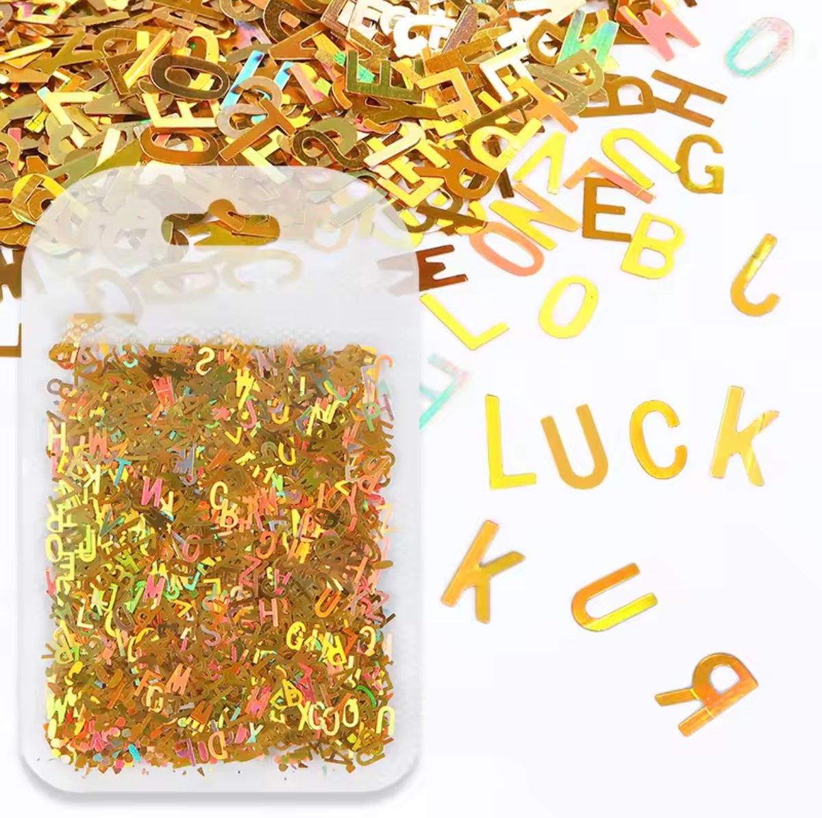 A clear plastic bag filled with gold foil letter confetti and scattered around on a white background, with additional gold foil letters visible inside the bag and some spilled over the side.