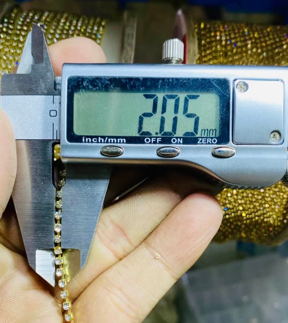 A close-up of a hand holding a gold chain with a digital caliper measuring it, showing a length of 20.5 mm on the screen.