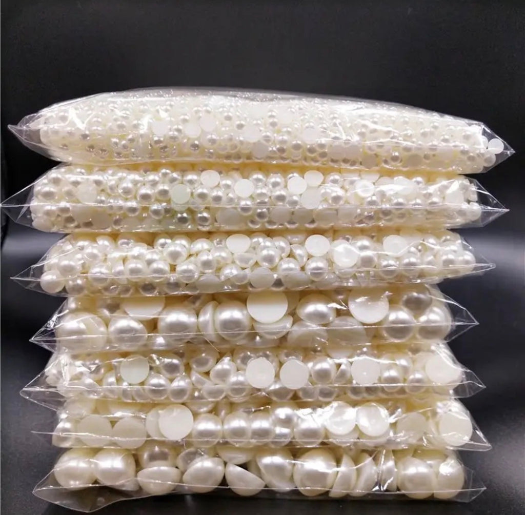 A stack of clear plastic bags filled with white faux pearl beads in various sizes, set against a dark black background.
