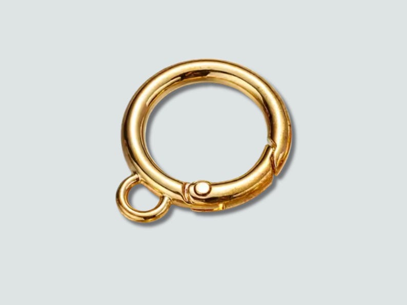 A polished gold-tone metal ring clasp with a small attached loop, shown on a light gray background.