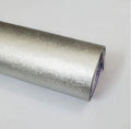 A close-up of a rolled metallic silver material, likely aluminum foil or a silver adhesive film, showing its textured reflective surface and purple backing layer.