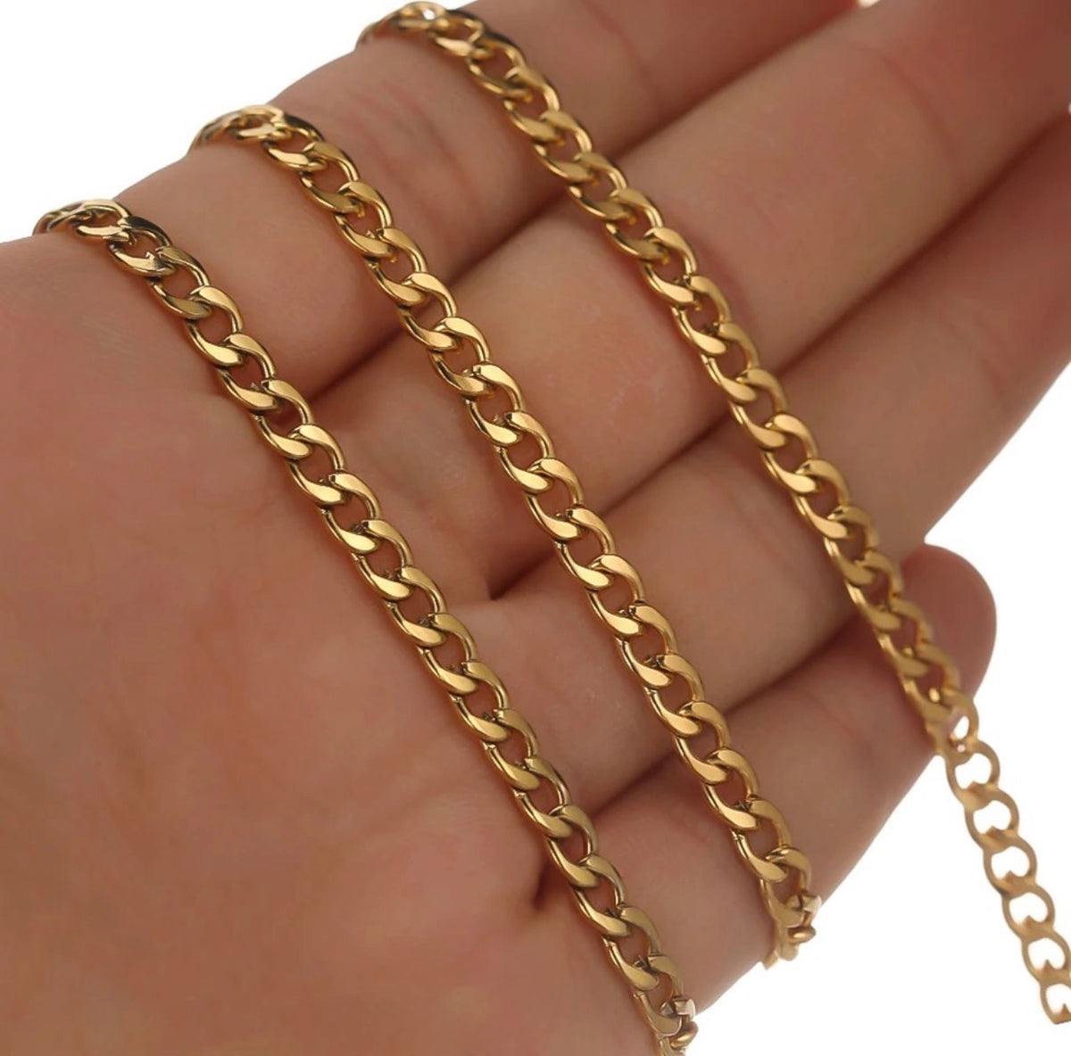 A close-up of a gold-tone Cuban link chain draped across a person's hand against a white background.