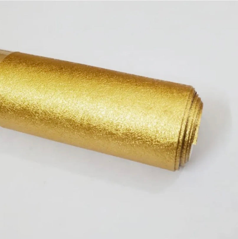 A roll of textured metallic gold craft vinyl or contact paper, shown diagonally on a plain white background.