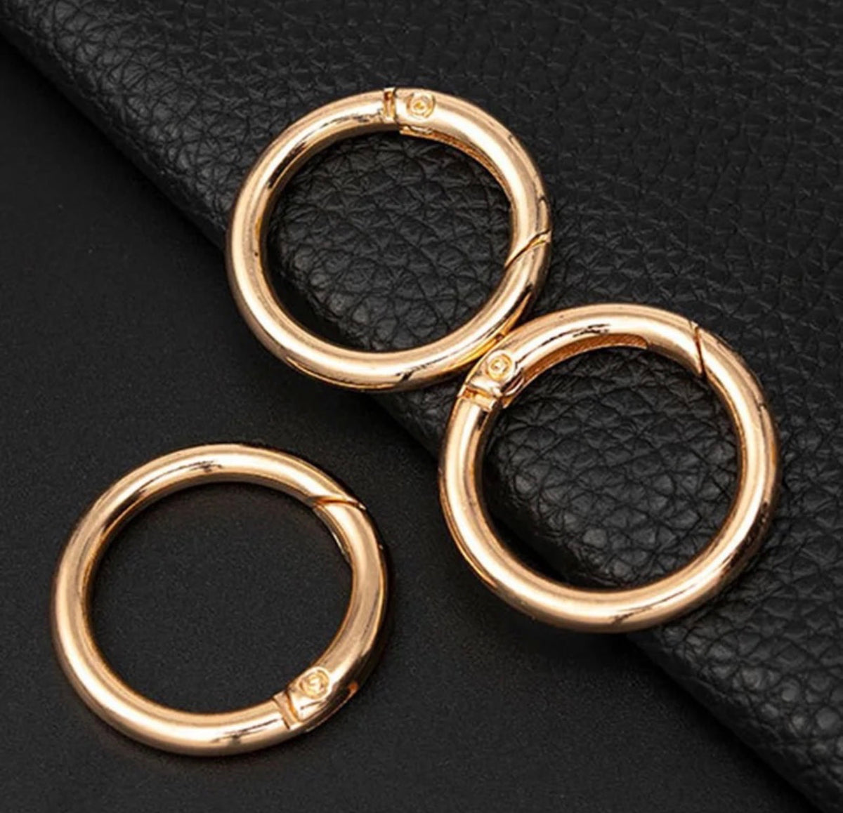Three gold-plated split ring clasps arranged on a textured black leather background.