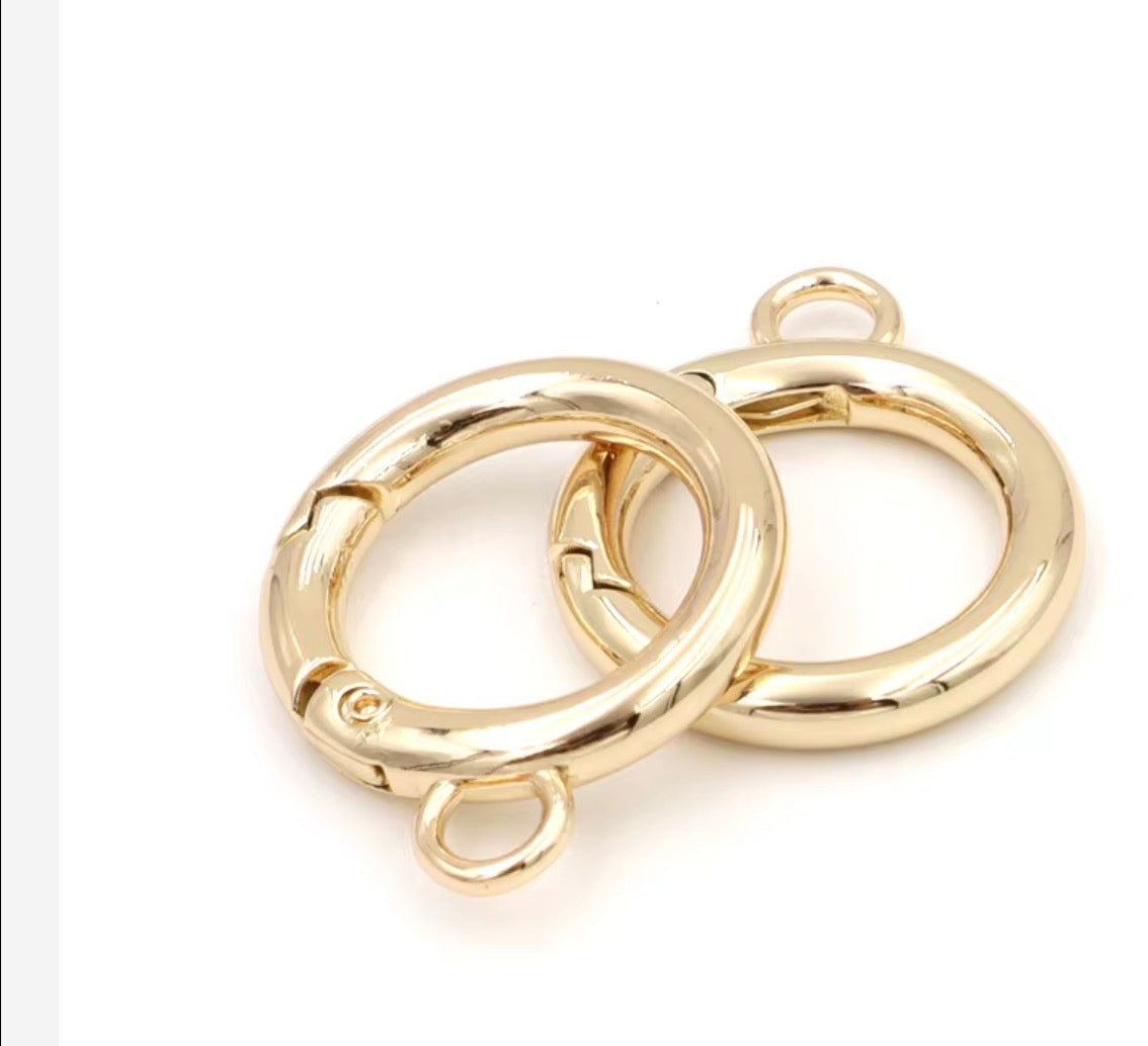 Two gold-plated metal jump rings with small loops on each end, shown overlapping on a plain white background.
