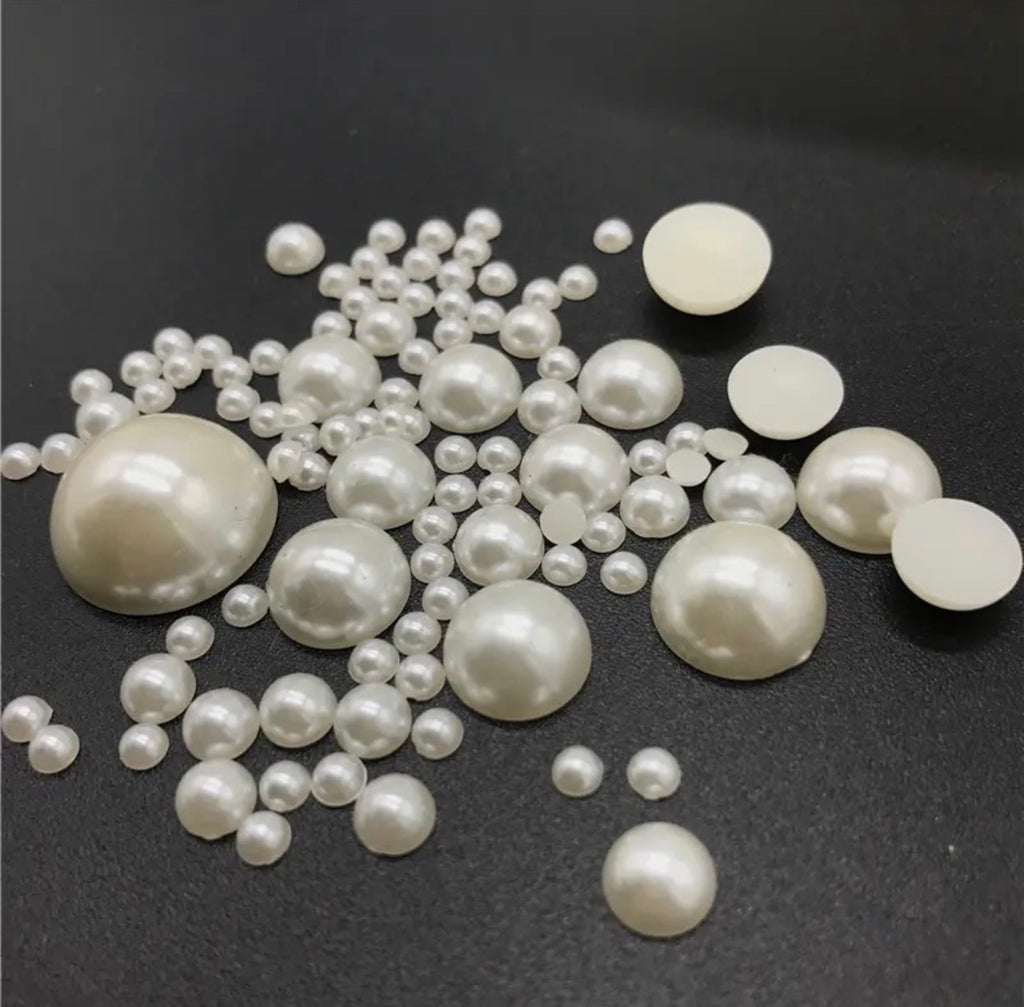 A collection of white faux pearl beads in various sizes, including flat discs and round glossy pearls, scattered on a dark gray background.