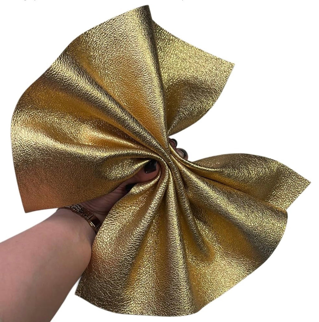 A hand holding a large, textured piece of metallic gold fabric against a plain white background.