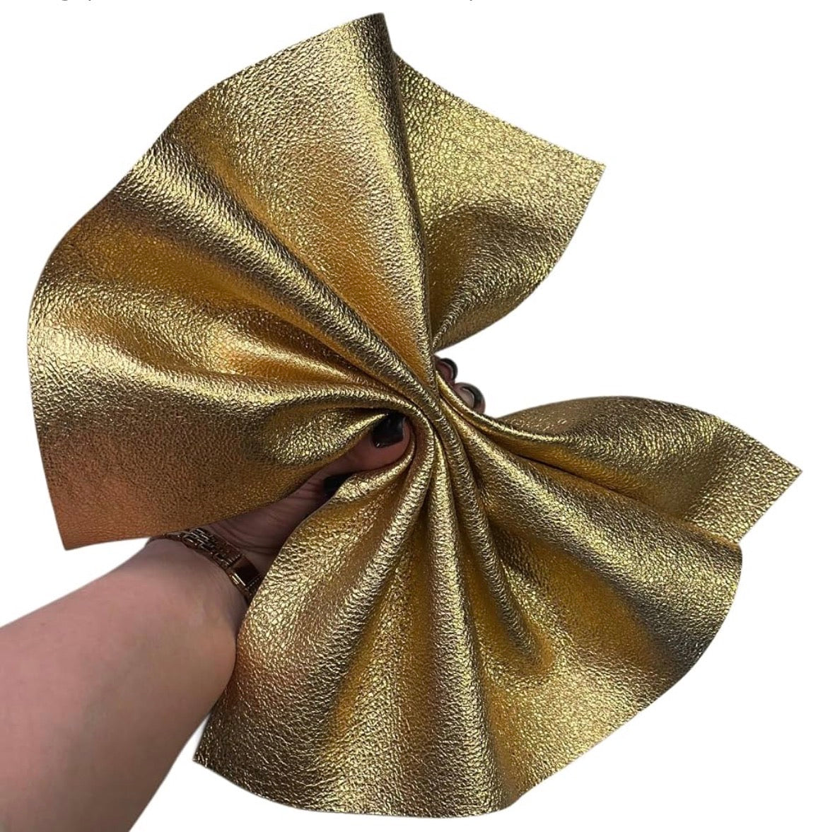 A hand holding a large, textured piece of metallic gold fabric against a plain white background.