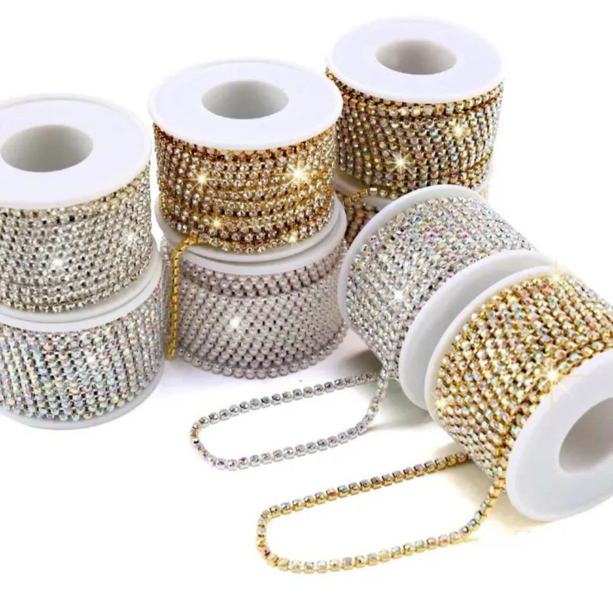 Several spools of rhinestone trim and bead ribbon on a white background, including silver, gold, and iridescent options with some loose strands displayed in front.