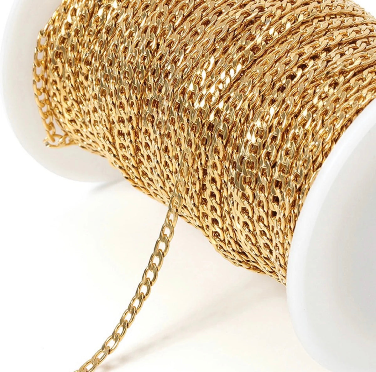 A close-up of a gold-colored chain draped over a white spool, showing the metallic links and texture of the chain against a clean white background.