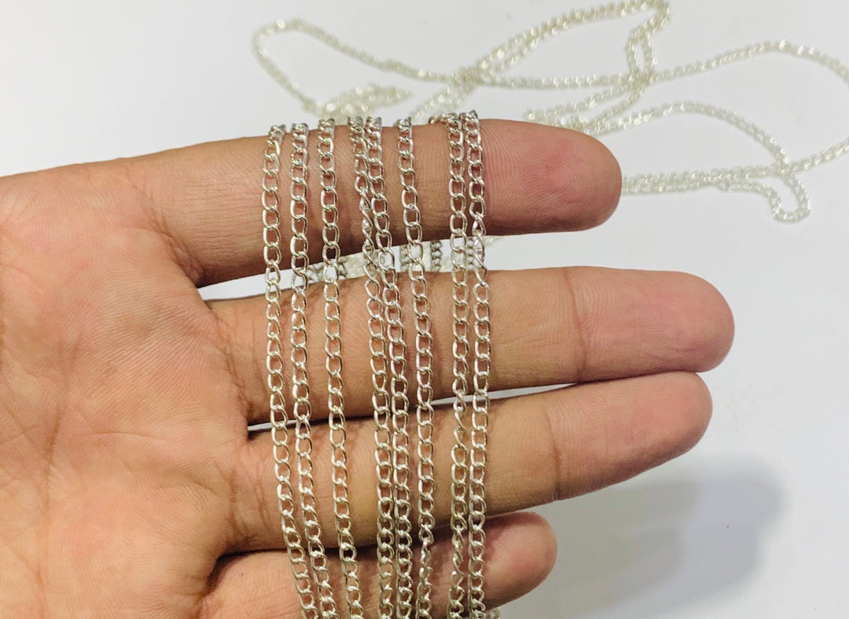 A close-up of a hand holding several strands of a silver-toned chain necklace against a plain white background.