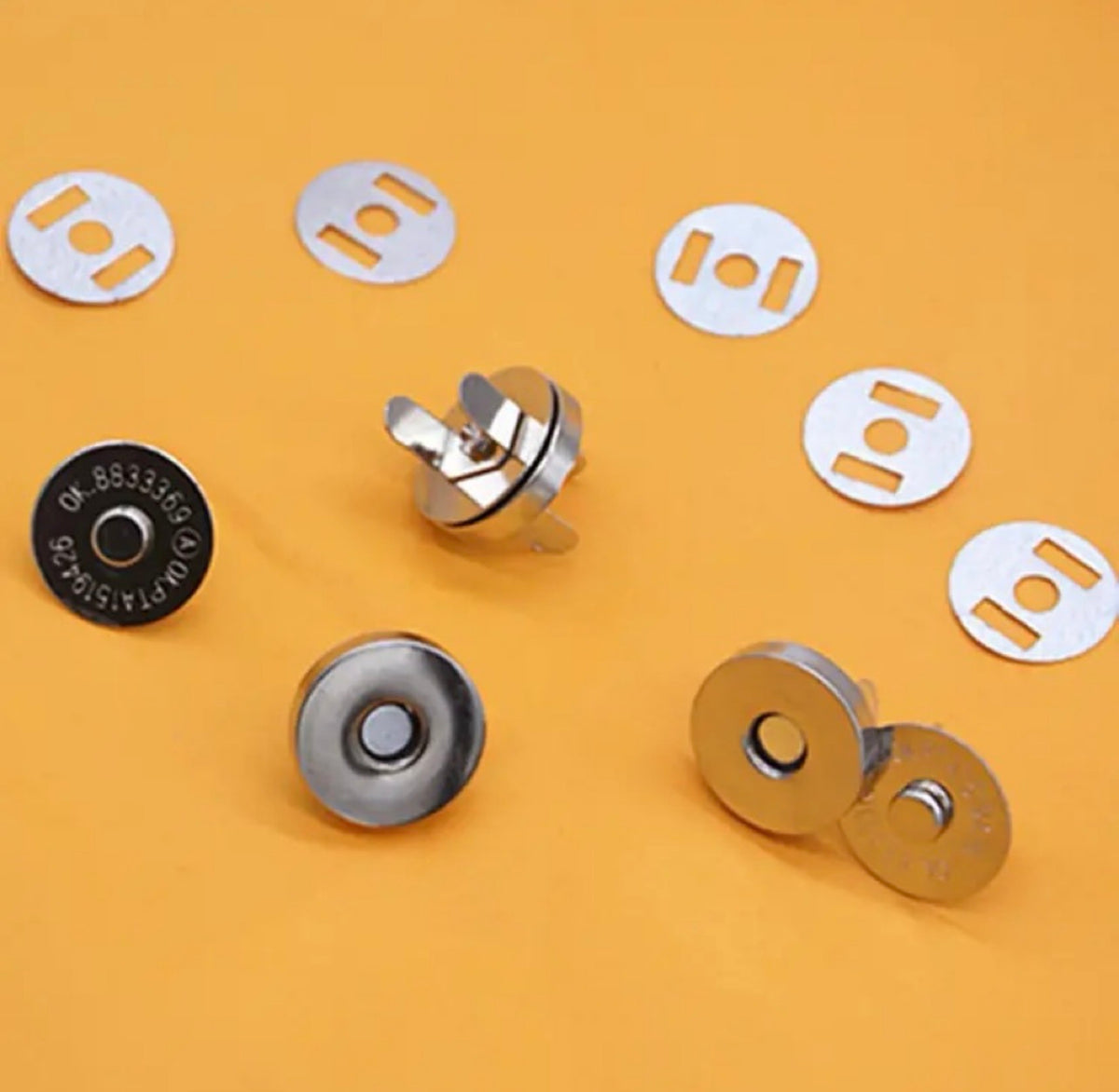 Small metal magnetic snap buttons and matching white plastic snap plates arranged on a solid orange background.