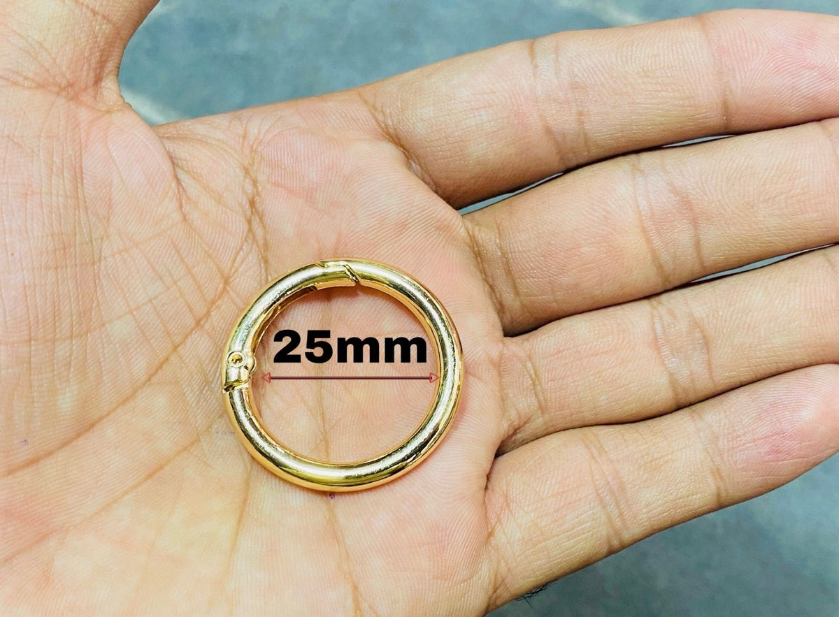 A gold-colored metal ring clasp or hoop shown resting on an open hand, with a black '25mm' size overlay printed over the center of the ring.