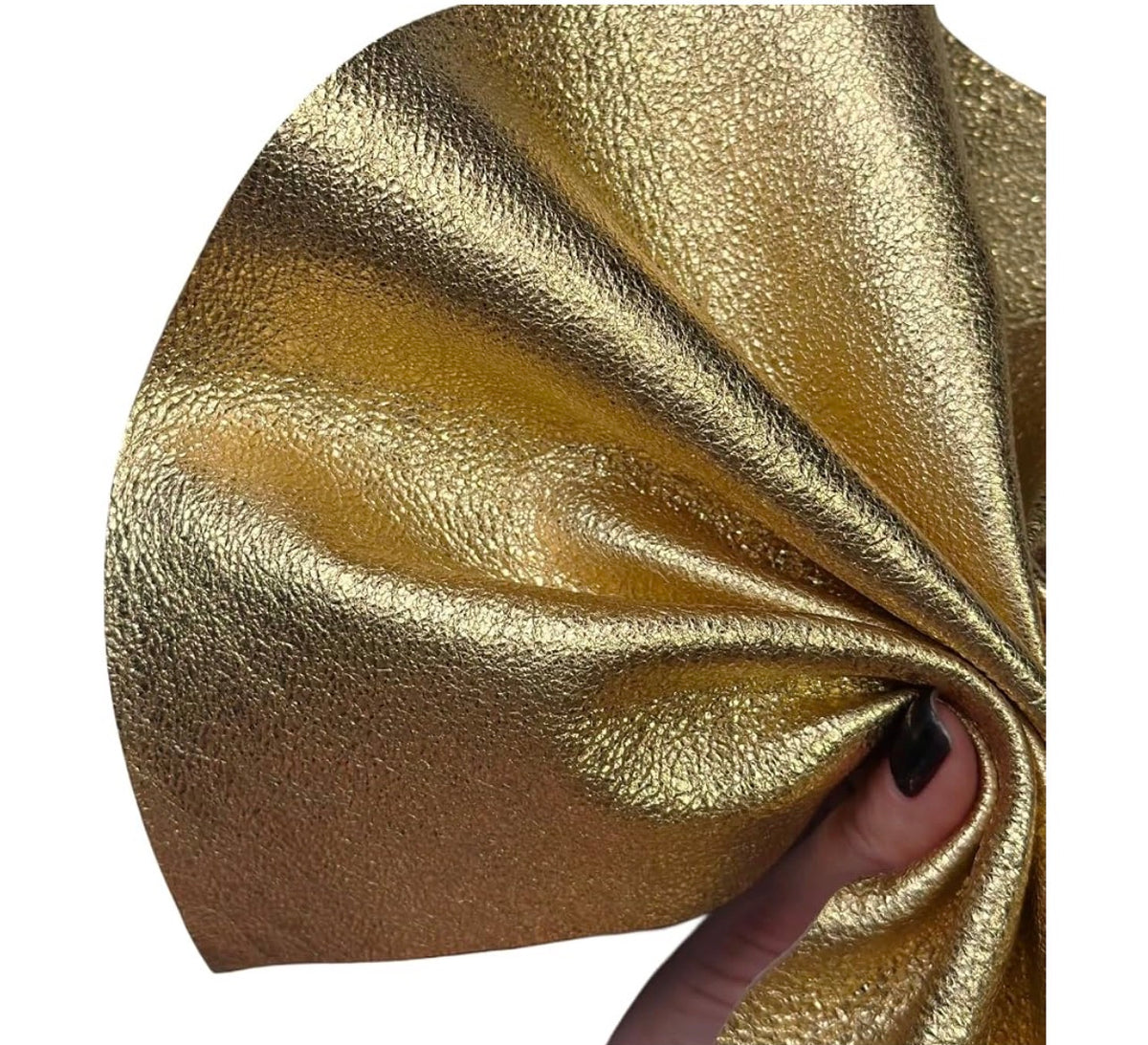 A close-up of shiny metallic gold textured material being gathered and stretched by a hand with black nail polish, on a plain white background.