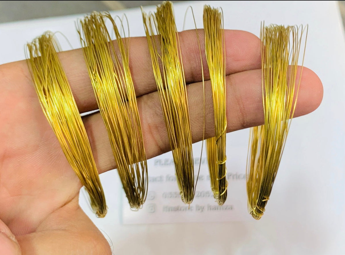Five small bundles of shiny gold-colored wire held in a person's hand against a white background.